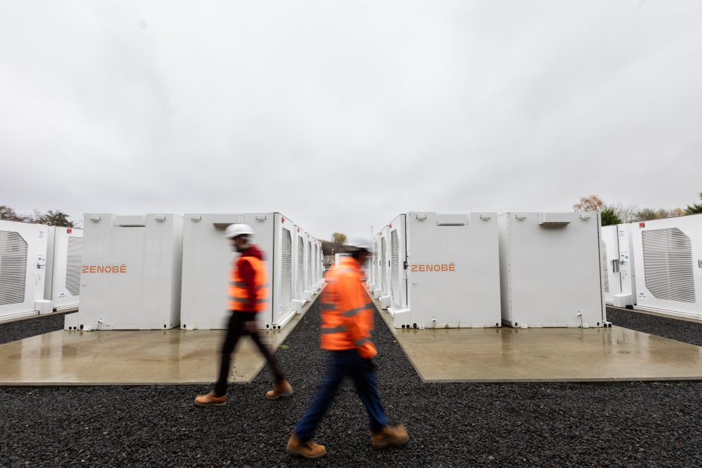 Two people in high visibility jackets walking past battery storage units