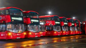 A row of red double-decker electric buses at night, parked at Transport UK London Bus’s depot, showcasing the fleet electrification partnership with Zenobē.