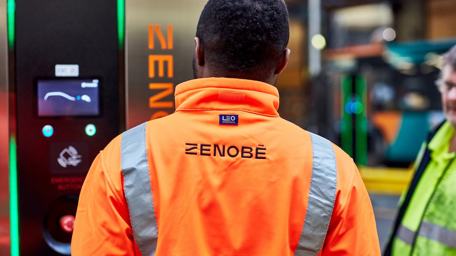 Man in orange high-viz standing in front of a Zenobe EV charger