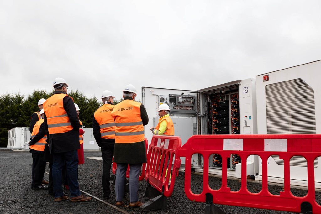 Zenobē team and visitors walking at the Wishaw battery storage site, showcasing key infrastructure for grid stability and renewable energy integration.