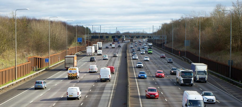 Busy UK motorway with cars, vans, and HGVs, representing the growing need for shared electric vehicle charging infrastructure.