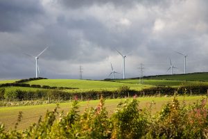 Wind turbines and electricity pylons on a green rural landscape under a dramatic cloudy sky.