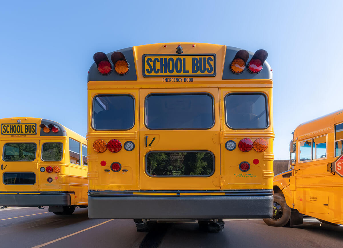 Rear view of a yellow electric school bus with emergency door and taillights visible.