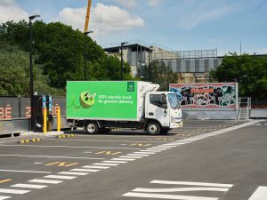 Electric delivery truck charging at a Zenobē shared charging hub for Woolworths in Australia, parked beside charging infrastructure in a marked depot area.